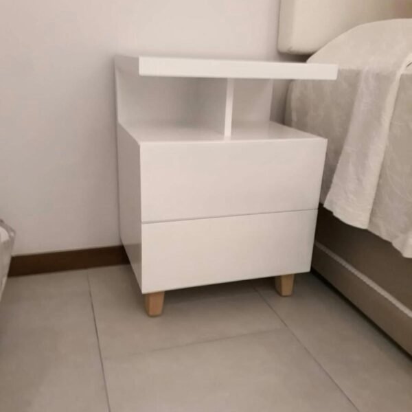 Mesa de luz blanca con dos cajones y nicho abierto junto a la cama